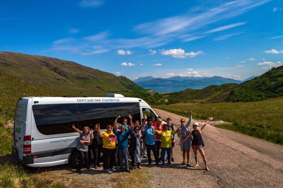 Group of people om tour with bus in background, hills and blue sky