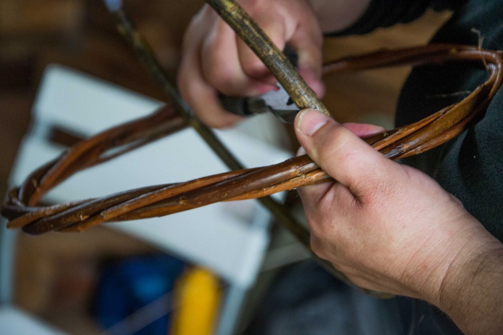 close-up of a pair of hands weaving 2 bits of thin wood together.