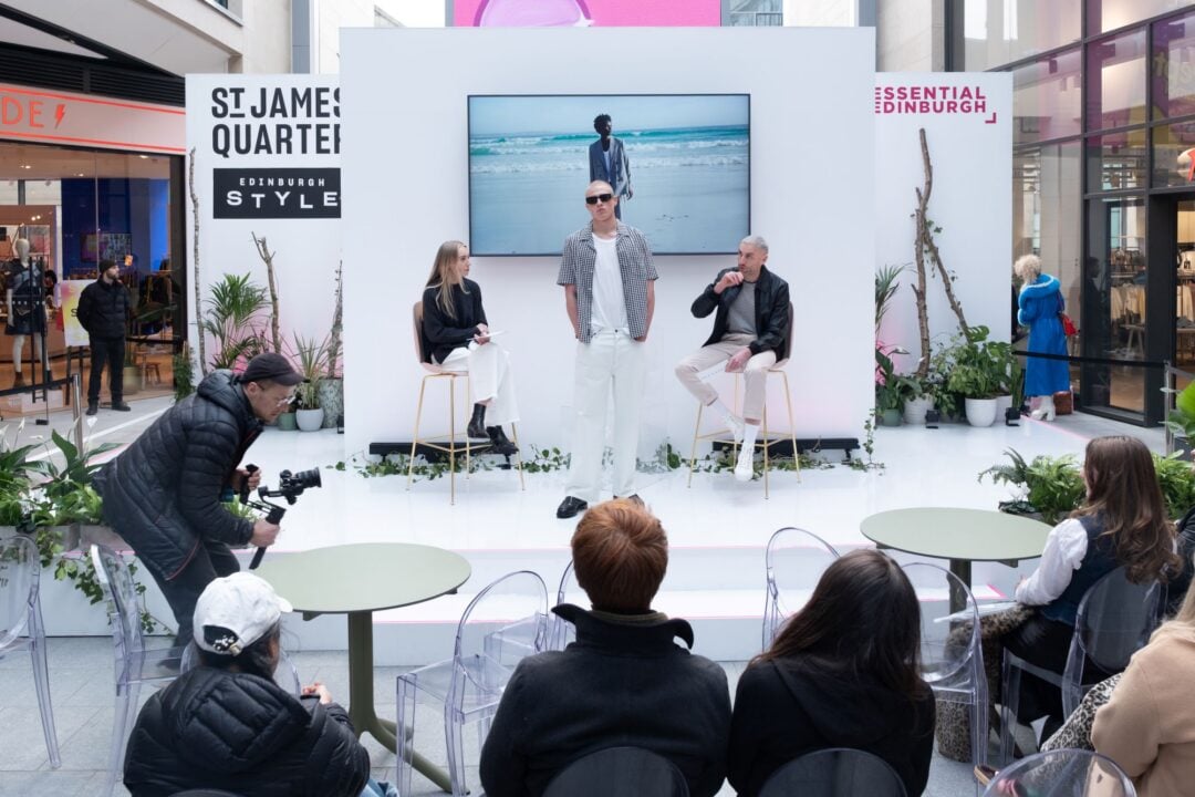 A model standing on a stage, in front of a group of people.