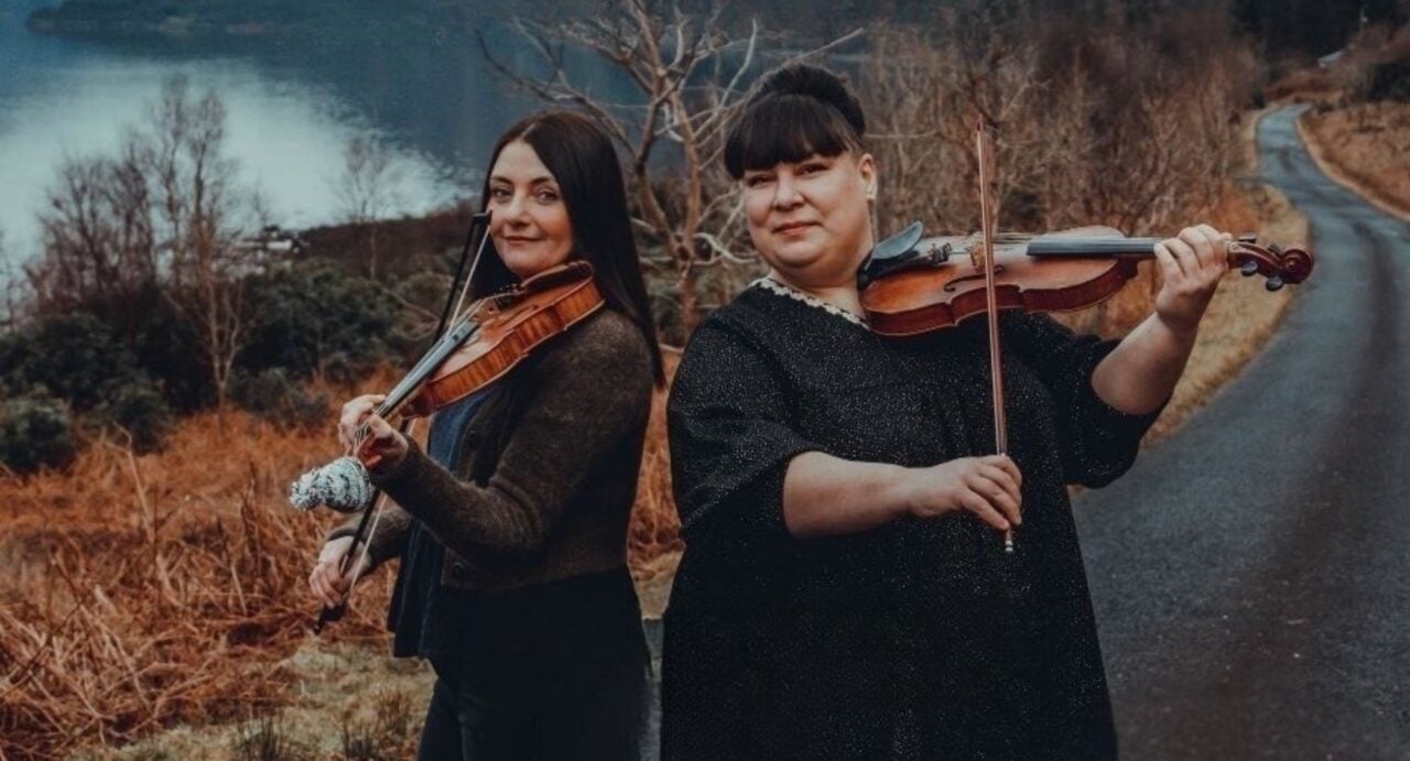 2 woman playing violins in an outdoor setting.