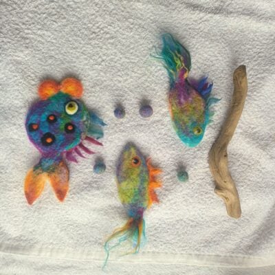 3 brightly coloured felt fish and a stick lying on a white cloth.