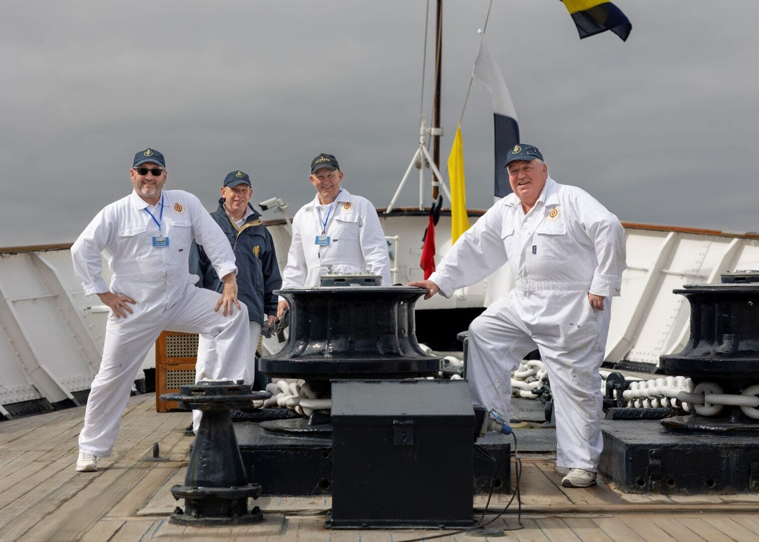 4 men in white overalls standing on the deck of a ship.