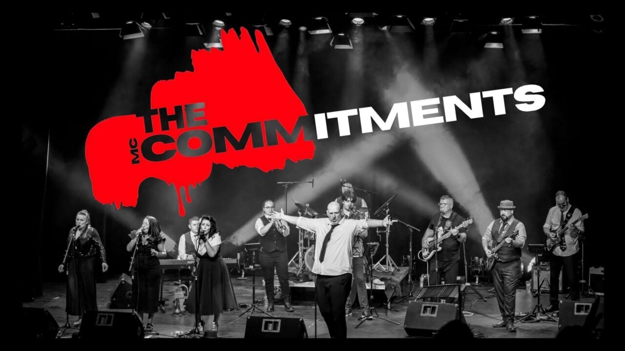 An 11-piece band, including 4 singers, performing on stage.