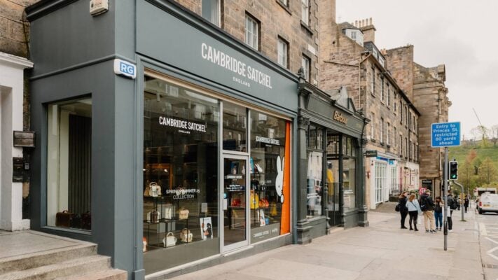 A modern storefront with wide glass windows and the name of the shop 'Cambridge Satchel' in white lettering over the doorway.