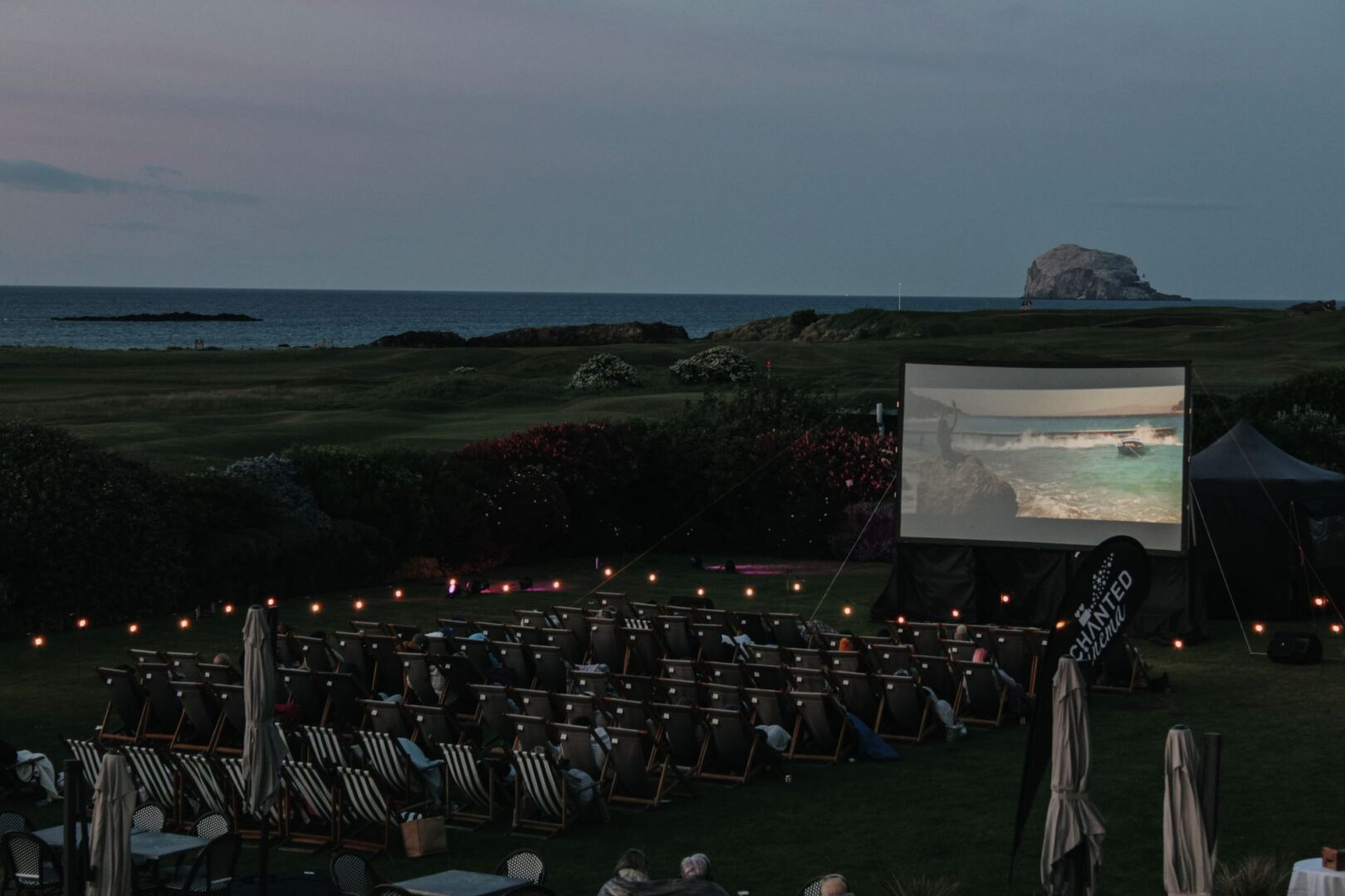Night time image of deckchairs set up in front of an outdoor movie screen.