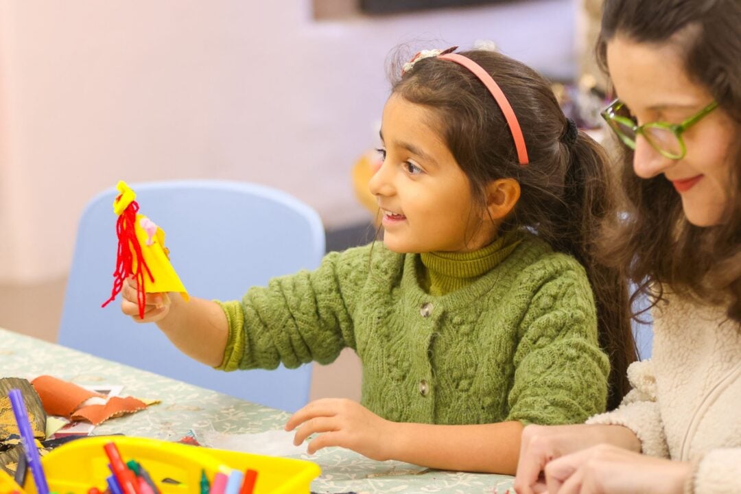 A young girl holding a peg doll, which has long red hair and a yellow dress.