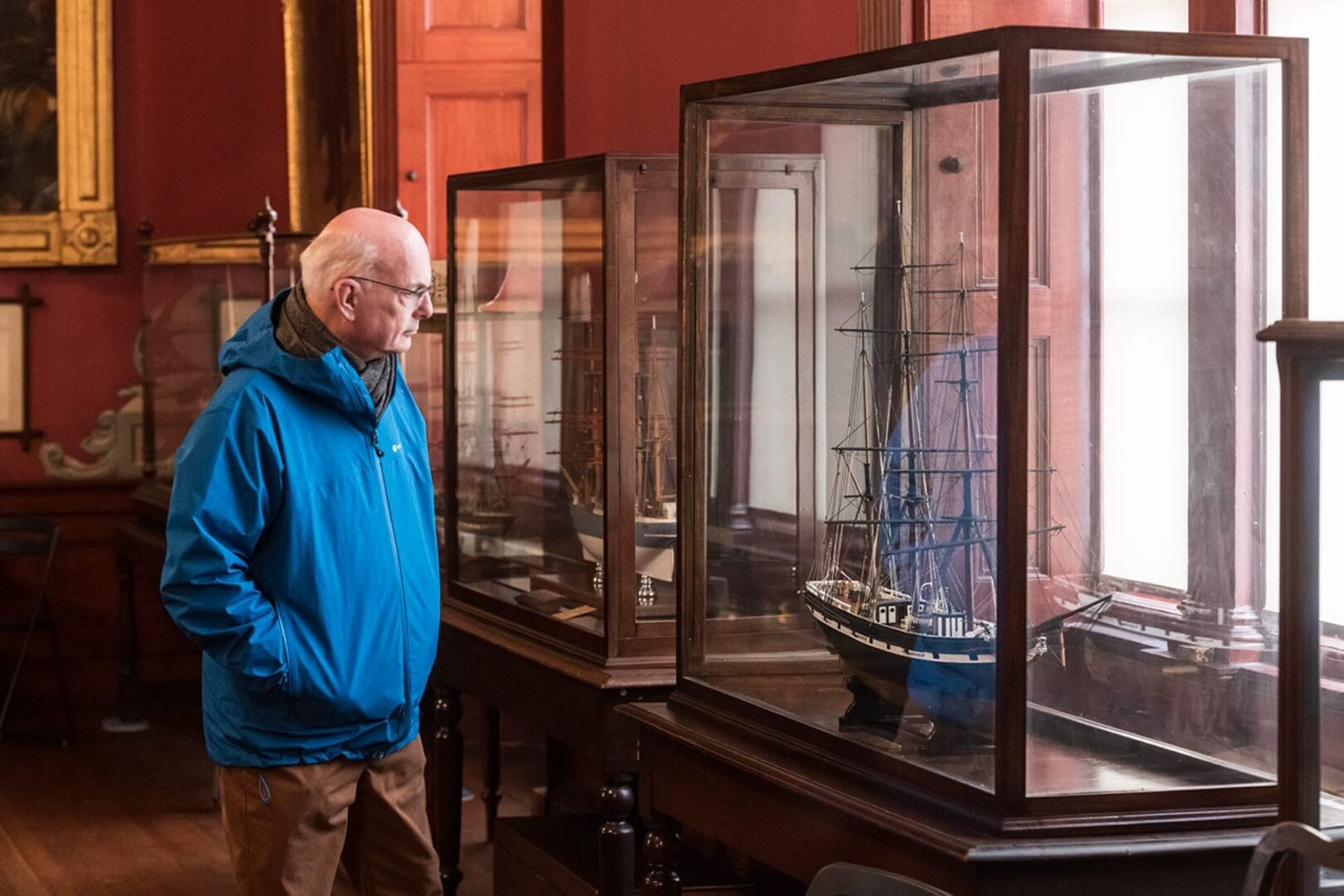 An elderly man looking at a display of a model ship, which is inside a glass cabinet.