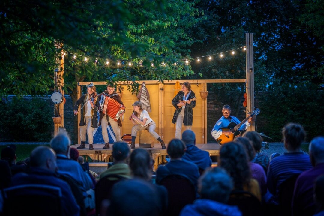 5 musicians performing on a outdoor stage in front of an audience.