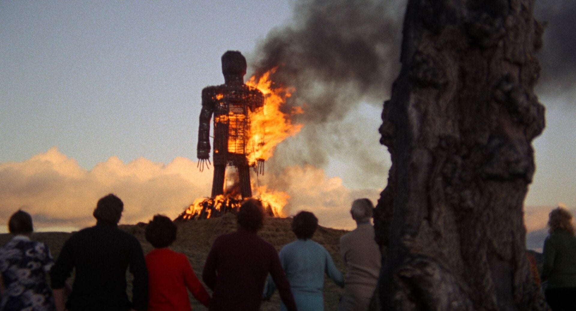 A burning wicker sculpture is watched by a group of people.