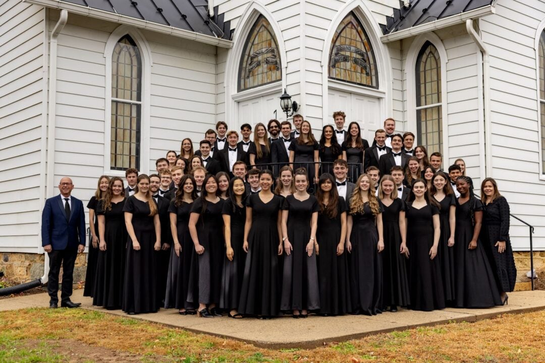 A group of people, all wearing black, standing outside a white building, with stained glass windows.