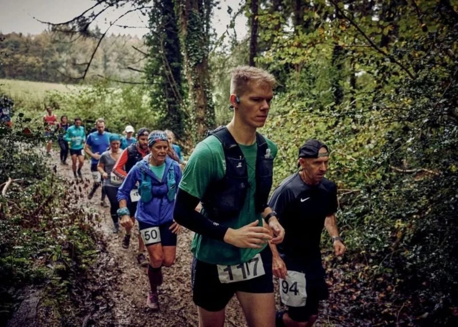 A group of people running through a wooded area.