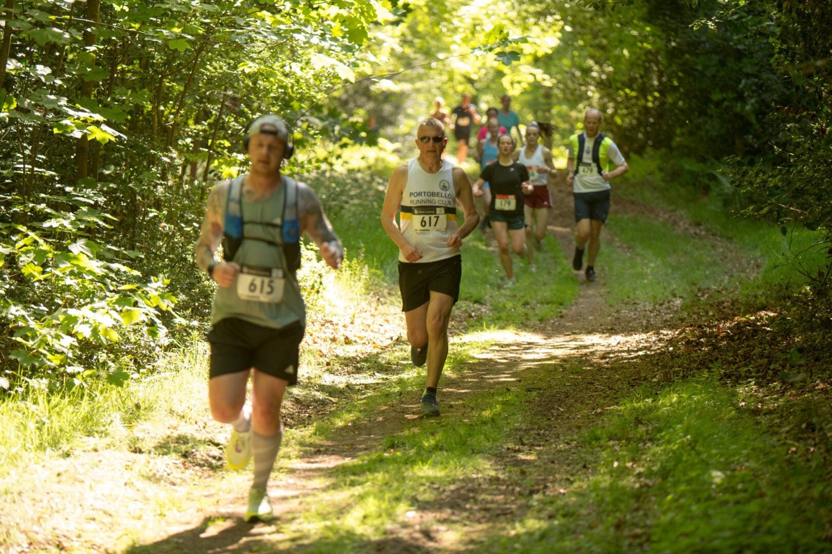 Runners running through a sunny wooded area.