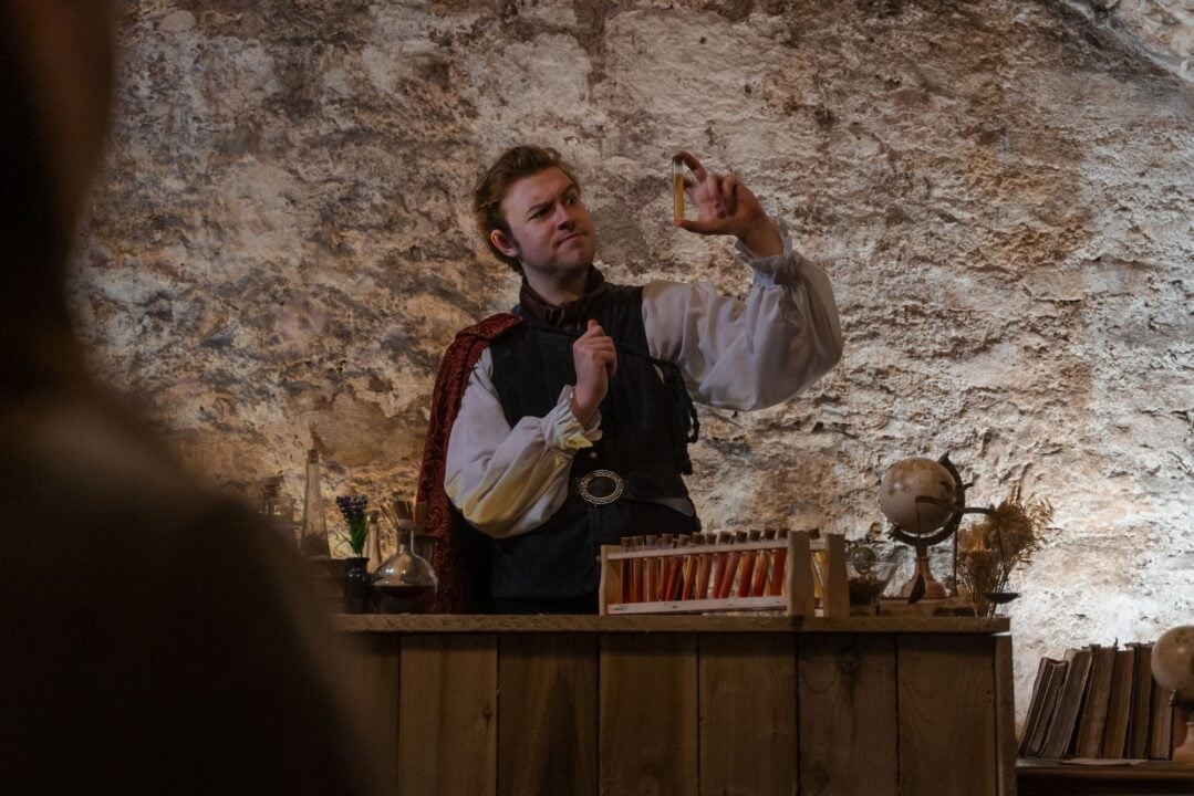 A man wearing old fashioned clothing, holding up a test-tube filled with liquid.