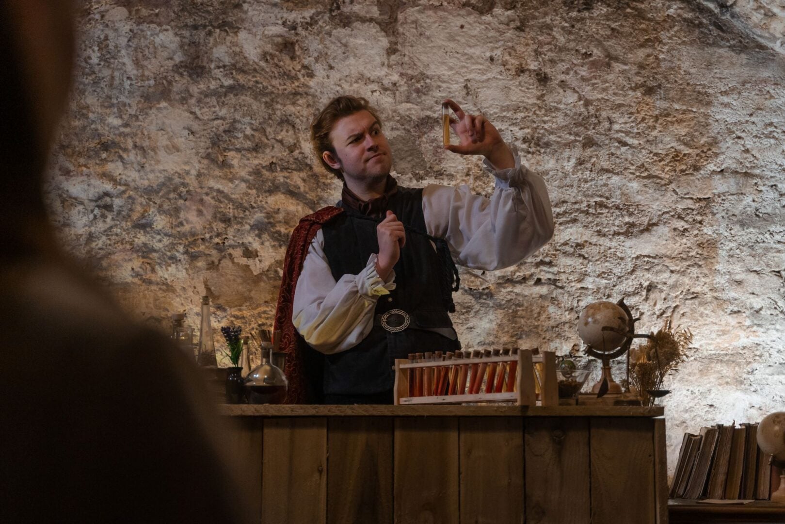 A man wearing old fashioned clothing, holding up a test-tube filled with liquid.