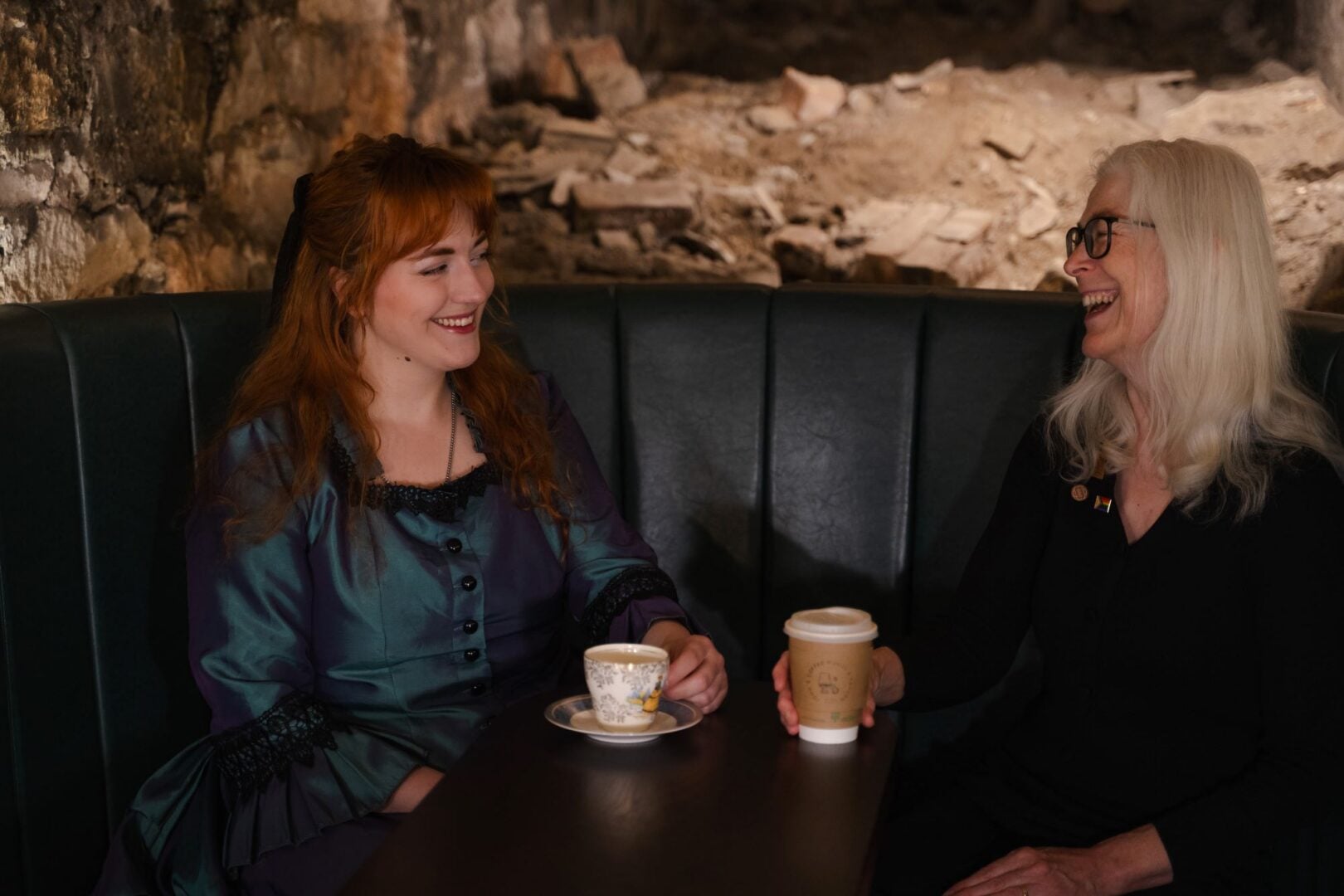 2 woman sitting a table, with drinks in front of them.