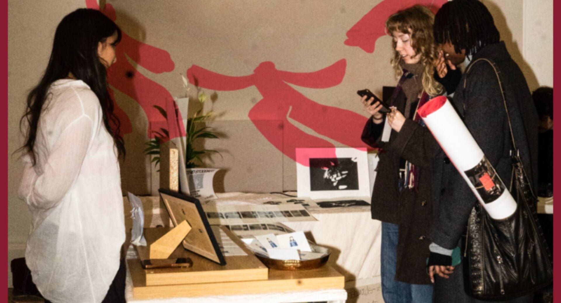 2 people look at a table and stand, on which are displayed prints and paintings.