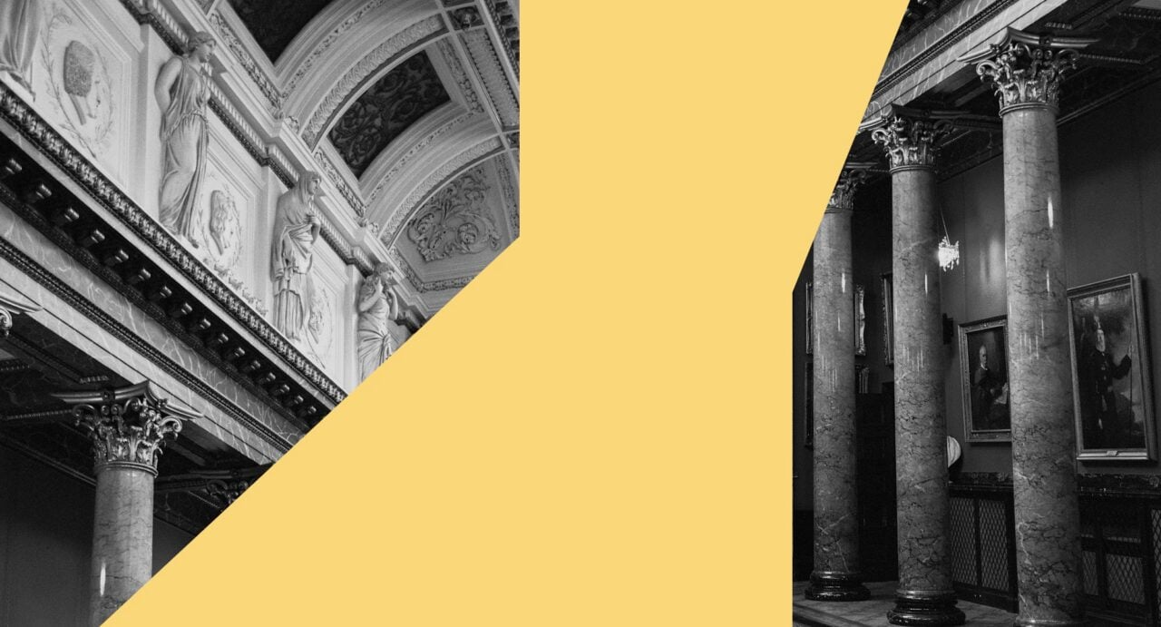 Black and white image of a grand hall, with marble columns and ornate ceiling, with yellow strip across centre of image.