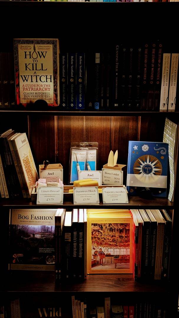 a dark bookcase showing books about witchcraft, history, and crafting supplies