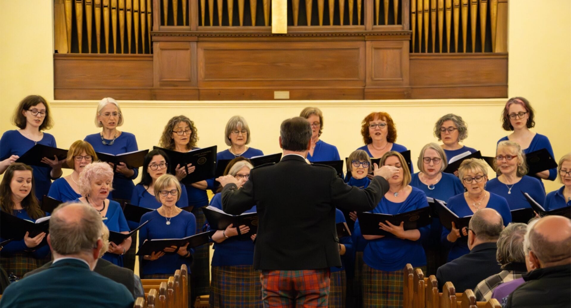 A group of people standing in front of a seated audience, singing.