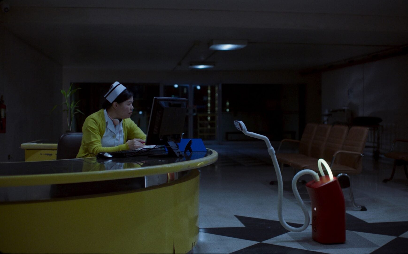 A nurse sitting at a desk, looking at hoover with a long hose.