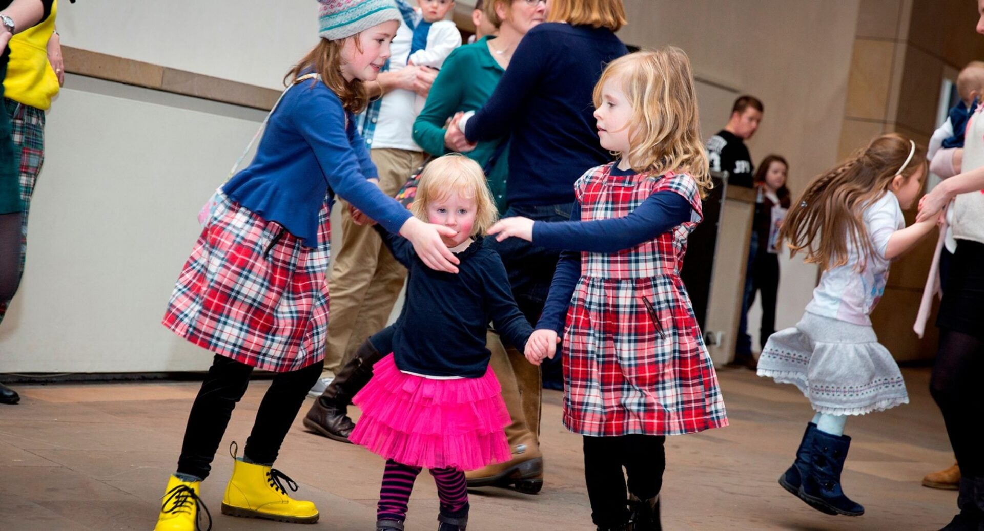 3 young girls, 2 wearing kilts, dancing in a circle.