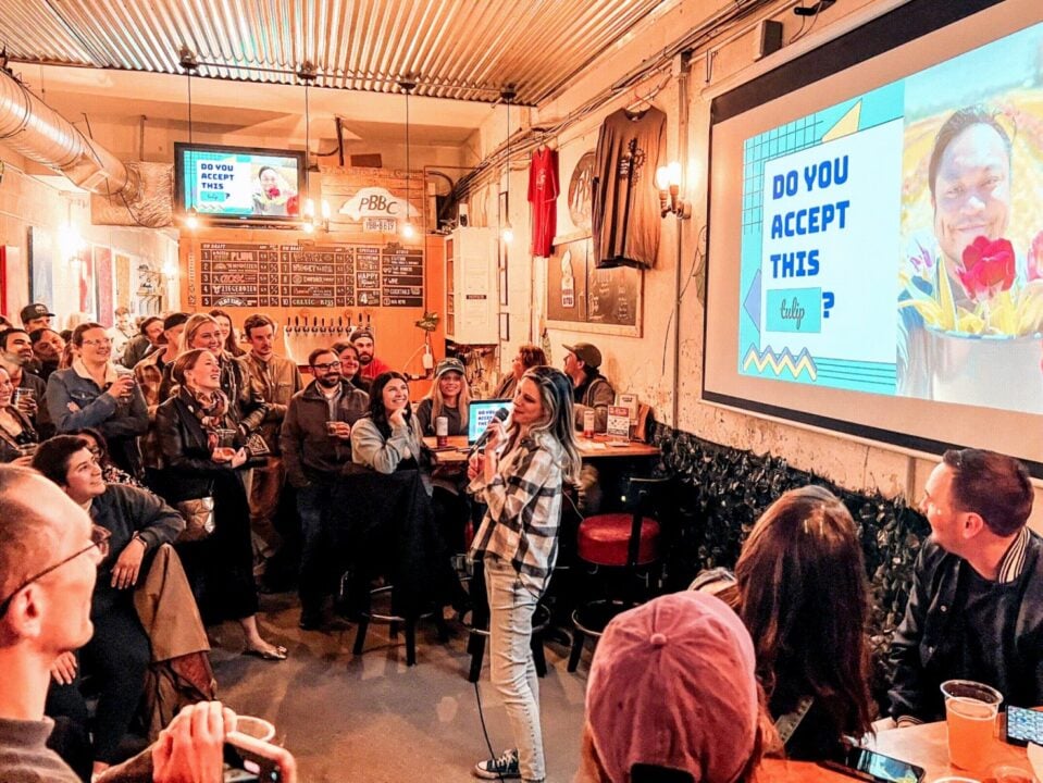 A woman holding a microphone, talking to a group of people in a bar.