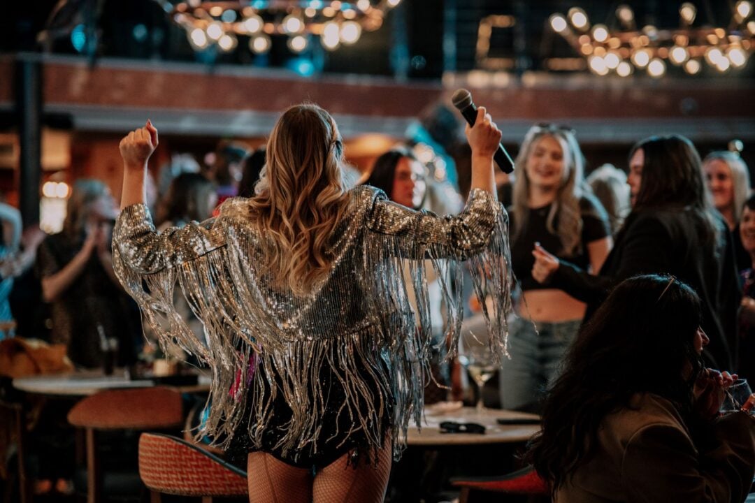 A person wearing a silver sparkly outfit performing in front of a bar of people.