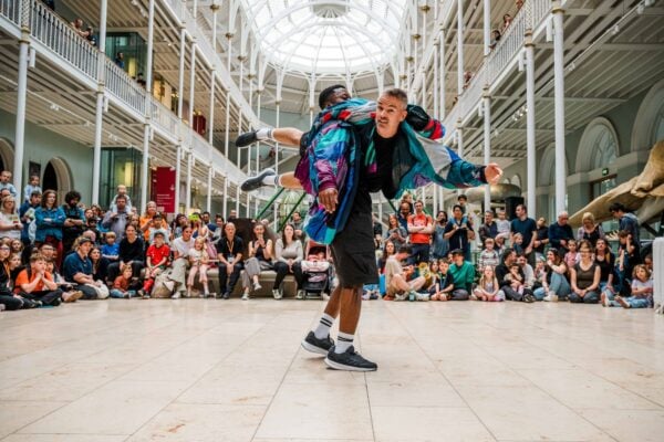 2 men whirling round, in front of a large crowd of people.