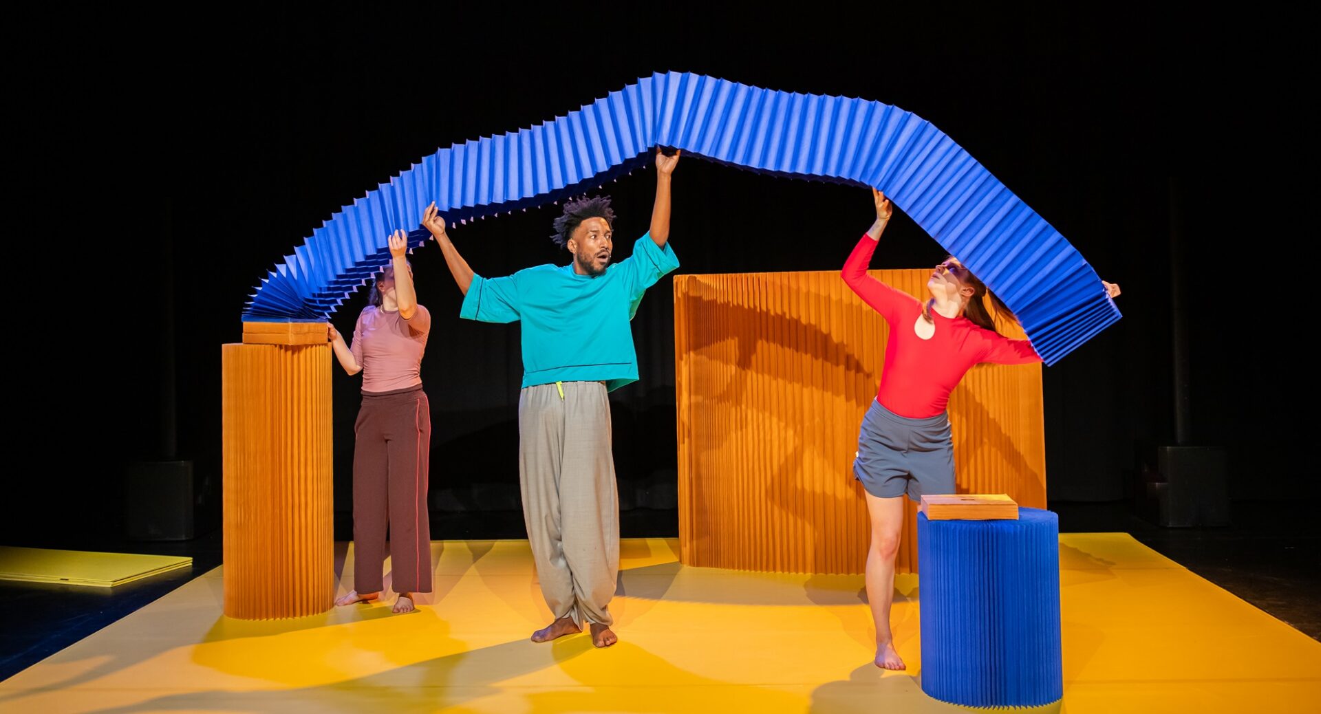 3 people holding a blue ribbon above their heads.