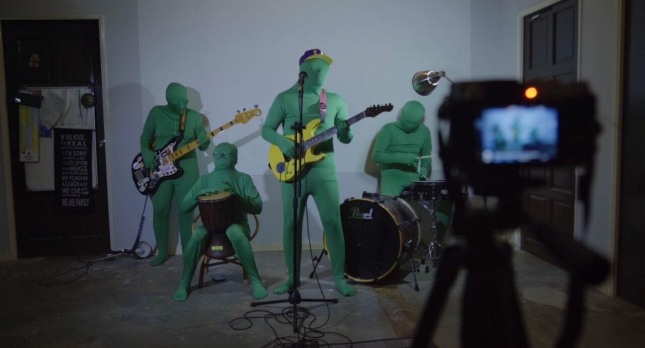 4 musicians in green suits performing in front of a camera.