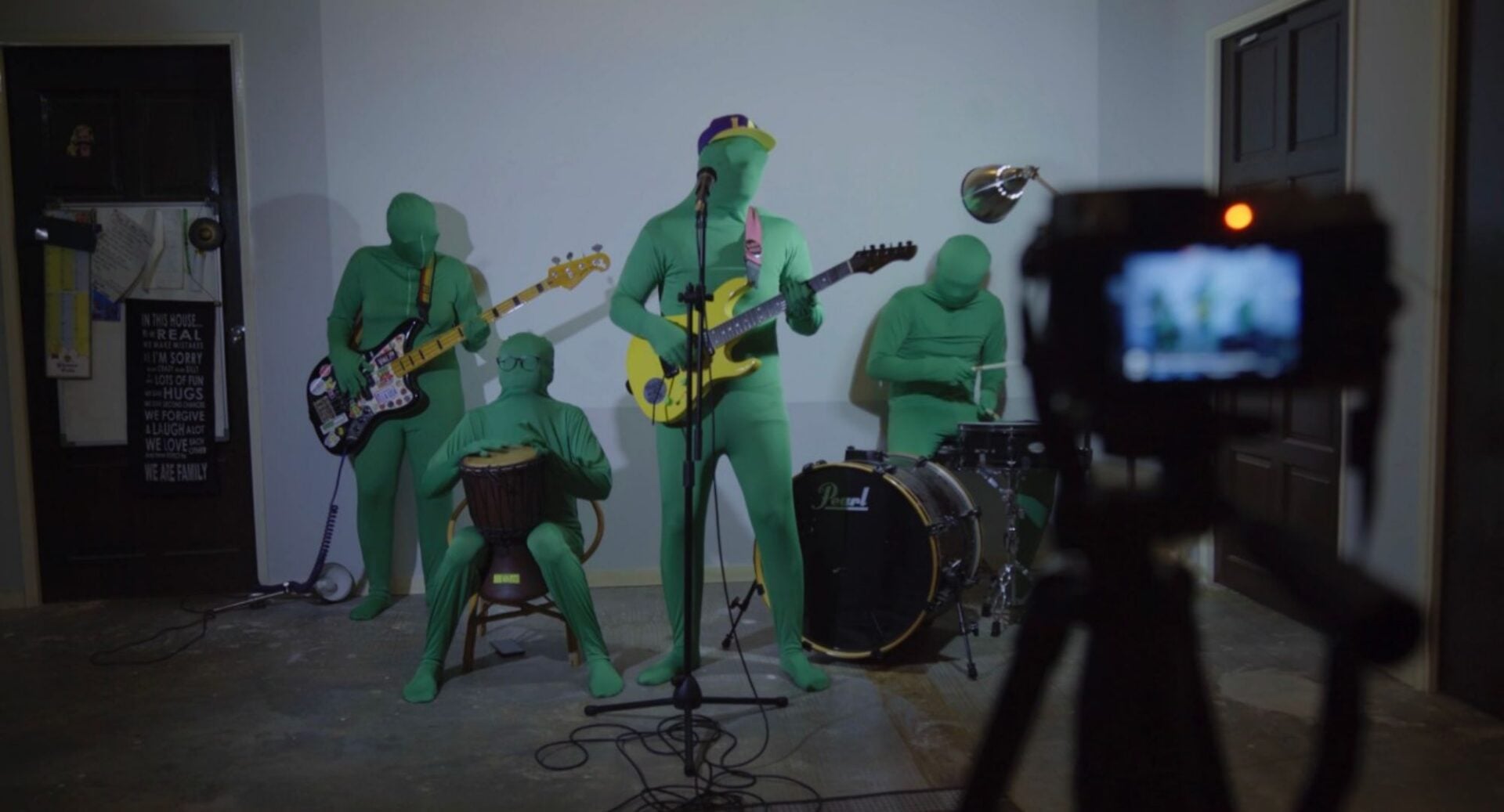 4 musicians in green suits performing in front of a camera.