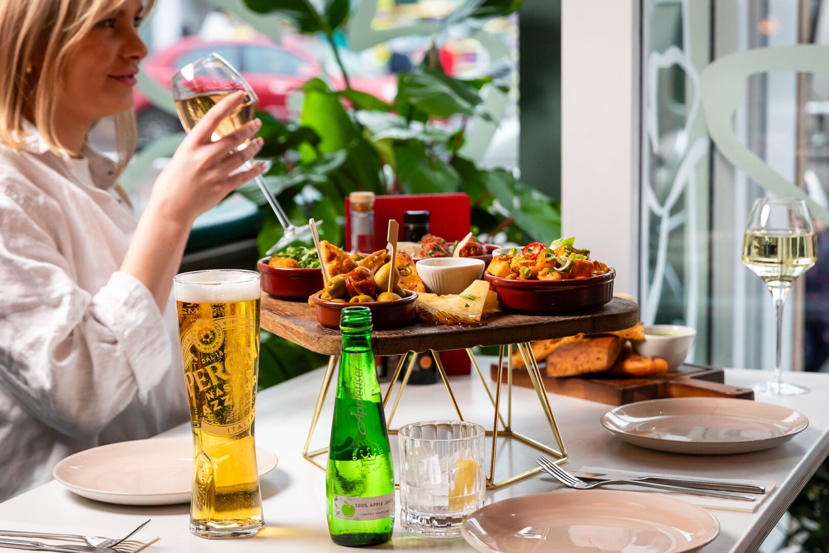 a lady sitting at a table, eating food and drinking wine.