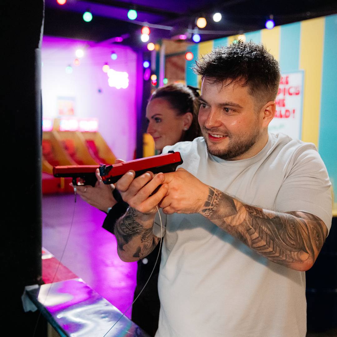Young couple shooting laser guns at fayre play