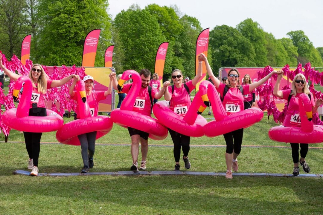 6 people all dressed in pink and wearing inflatable pink flamingos crossing a finishing line.