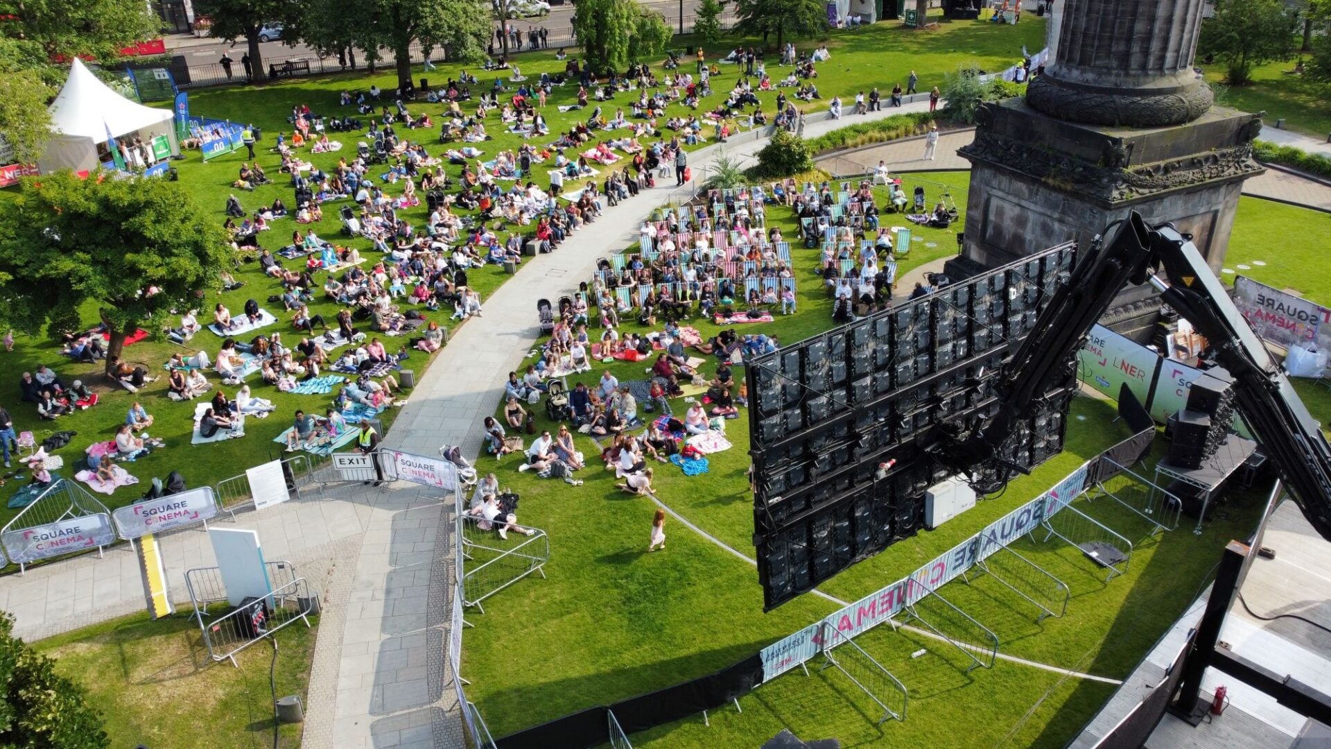 Birds--eye view of a large grassy area, with people watching a large cinema screen.