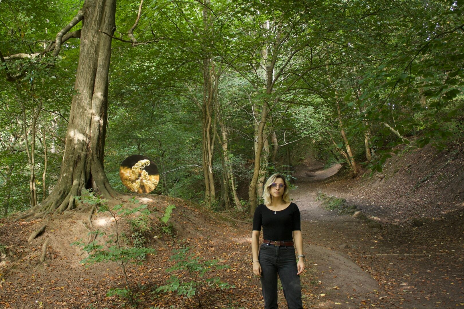 A woman standing in a wooded area, surrounded by trees.