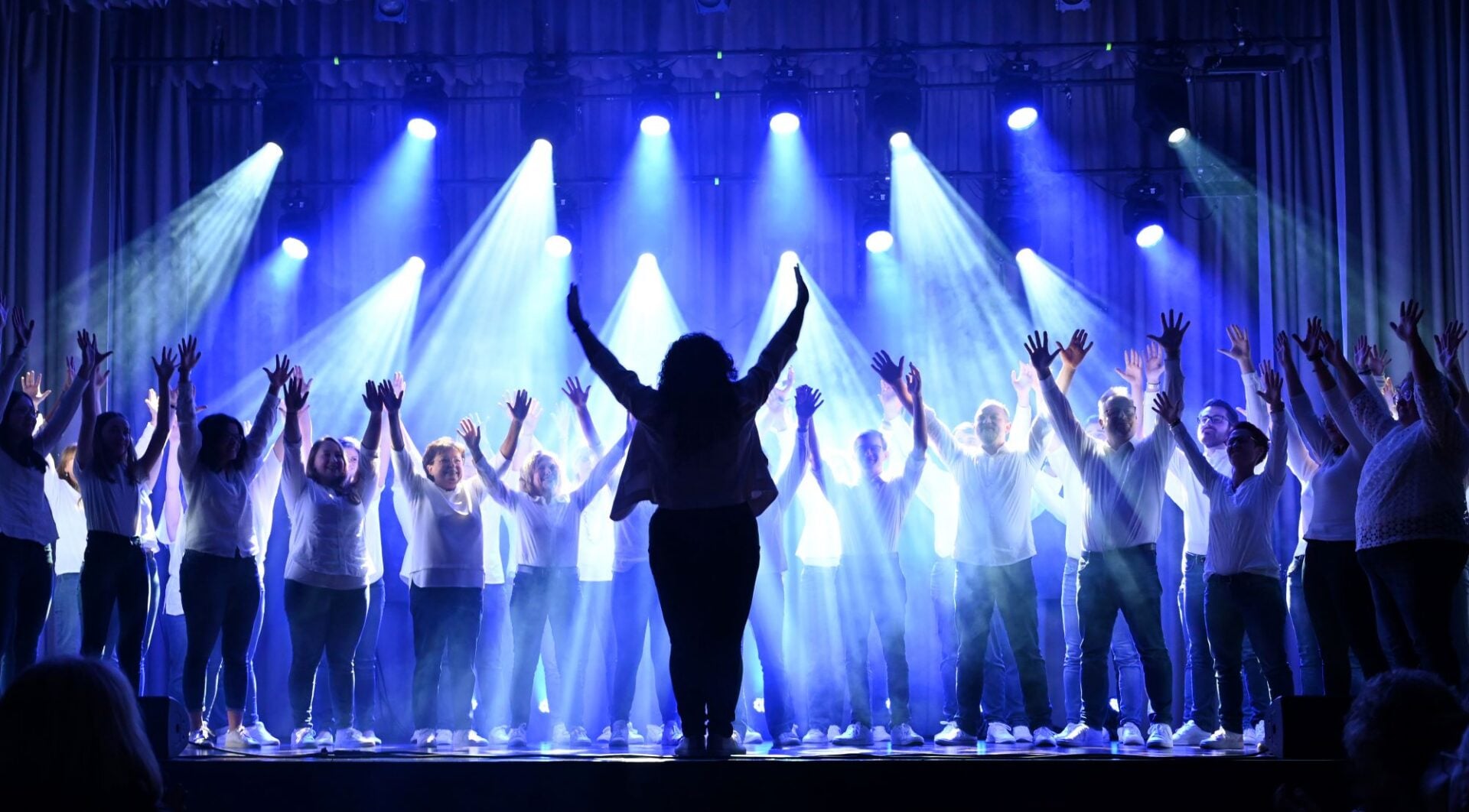A group of people singing on a flood-lit stage.