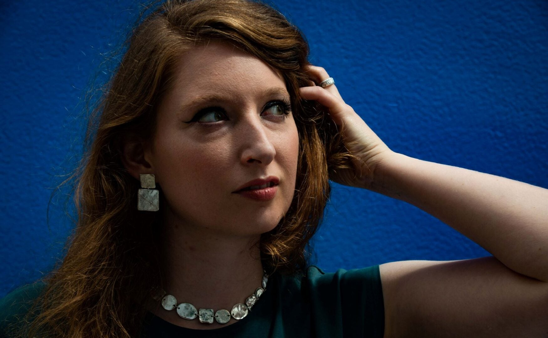 Woman with long brown hair, wearing a silver necklace and matching earrings.