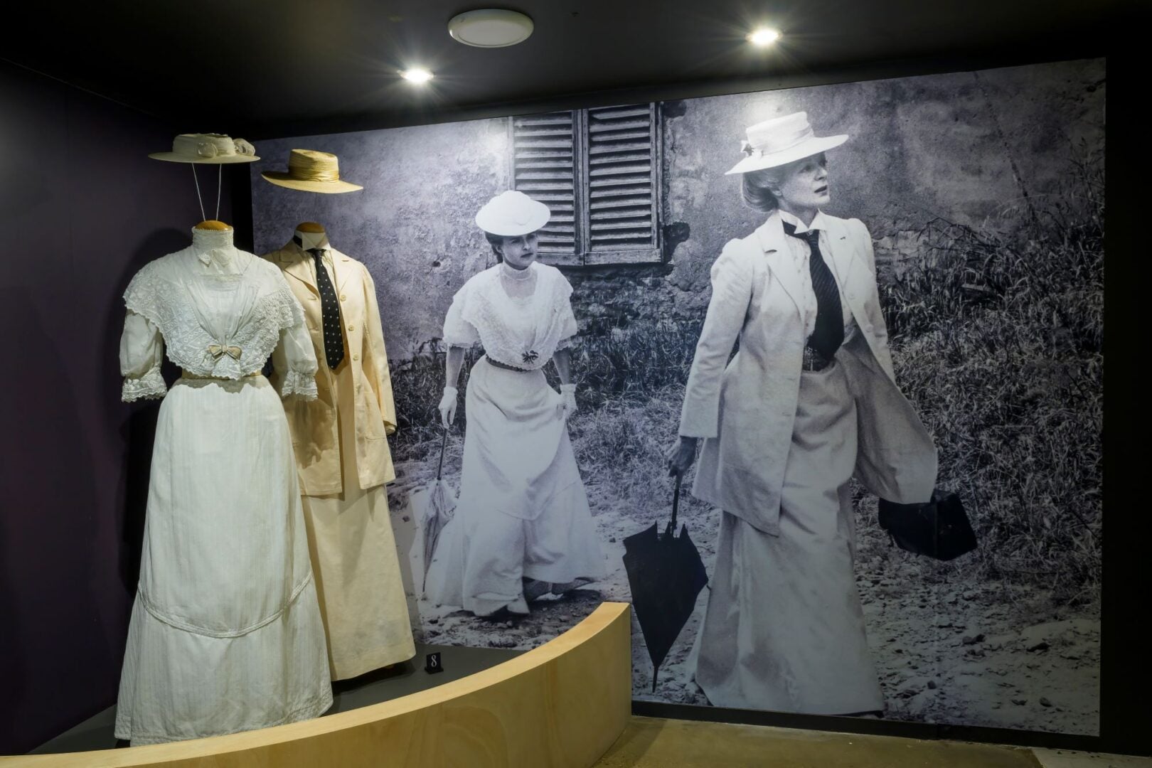 A black and white photo with 2 women, behind a display of 2 dresses.