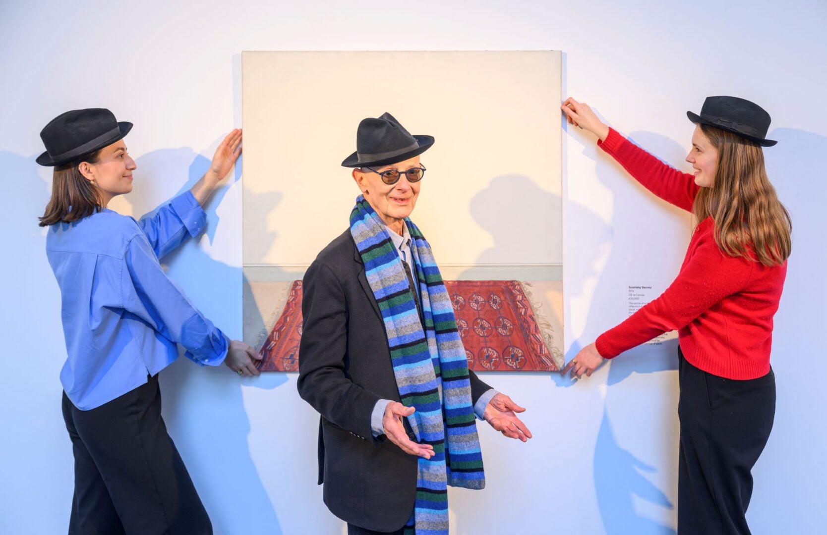 A man standing in front of a painting, which is being held on either side by a woman.