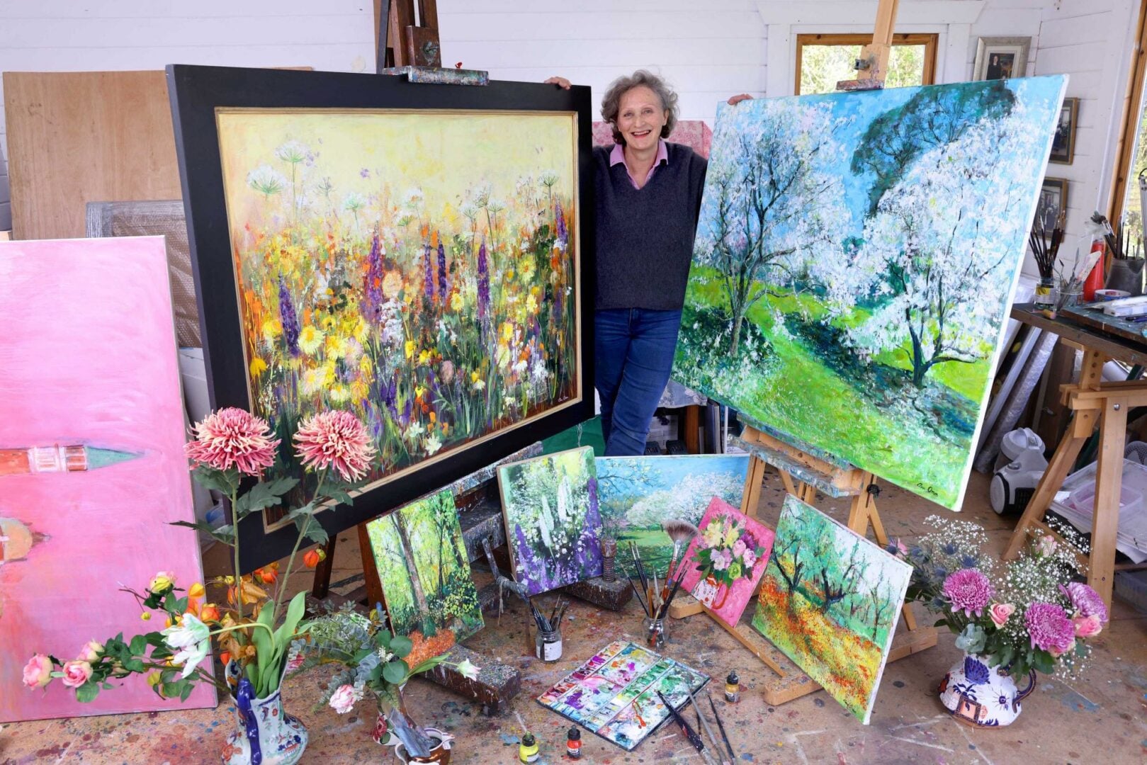 Woman standing in a room, surrounded by painted easels and painting equipment.