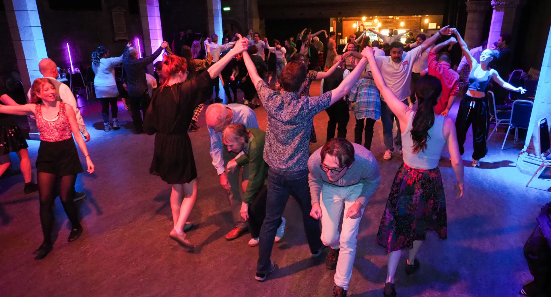 People dancing together in a dark space, with illuminated lighting.