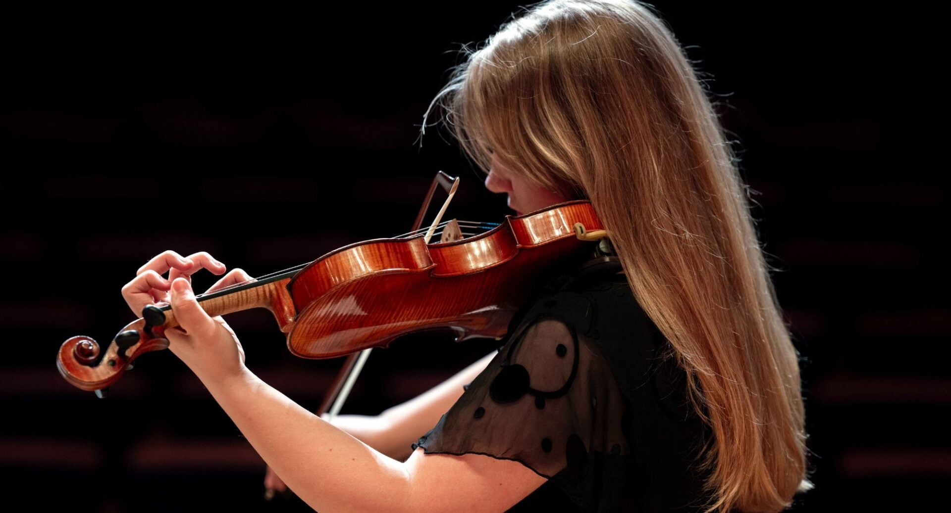 Side profile of a woman with long blonde hair playing a violin.