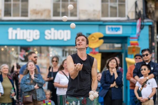 Man juggling balls, surrounded by a group of people watching.