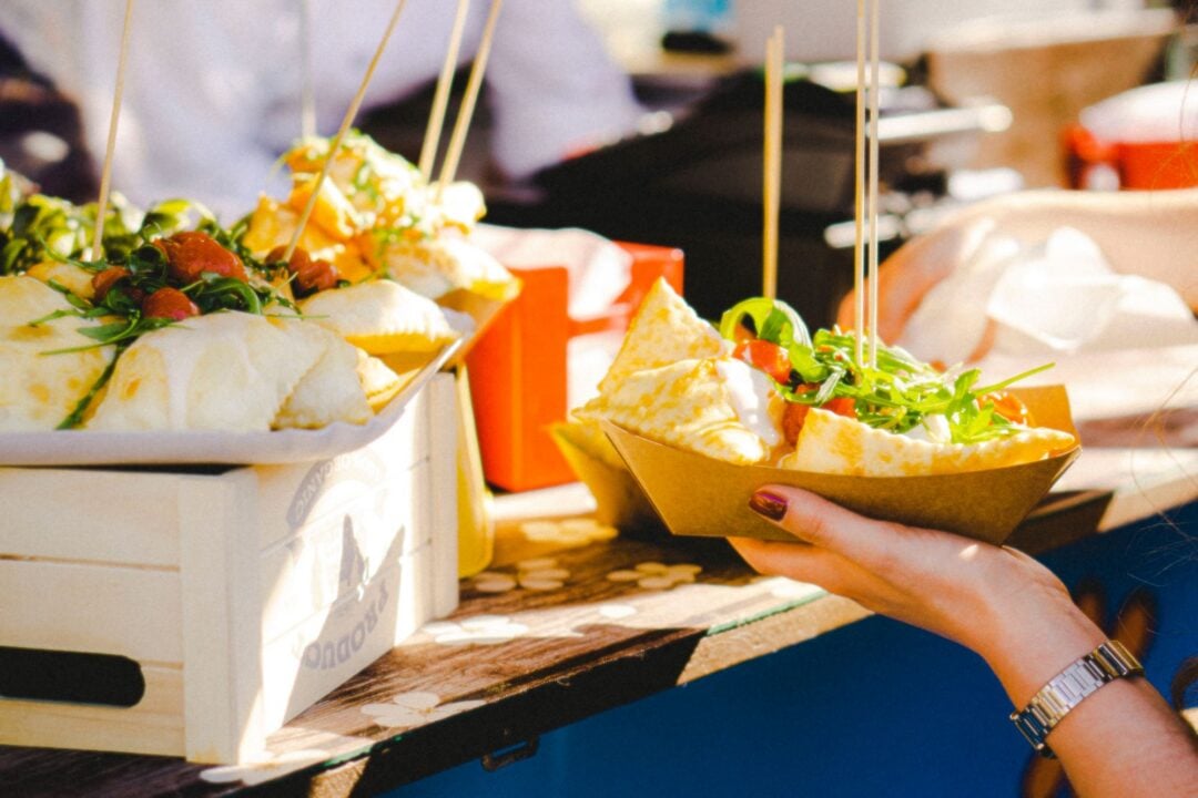 A hand taking a dish of food from a table.
