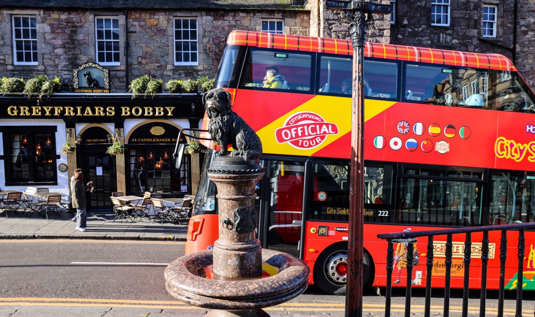 A red open-top tour bus going past a small bronze statue of a dog.