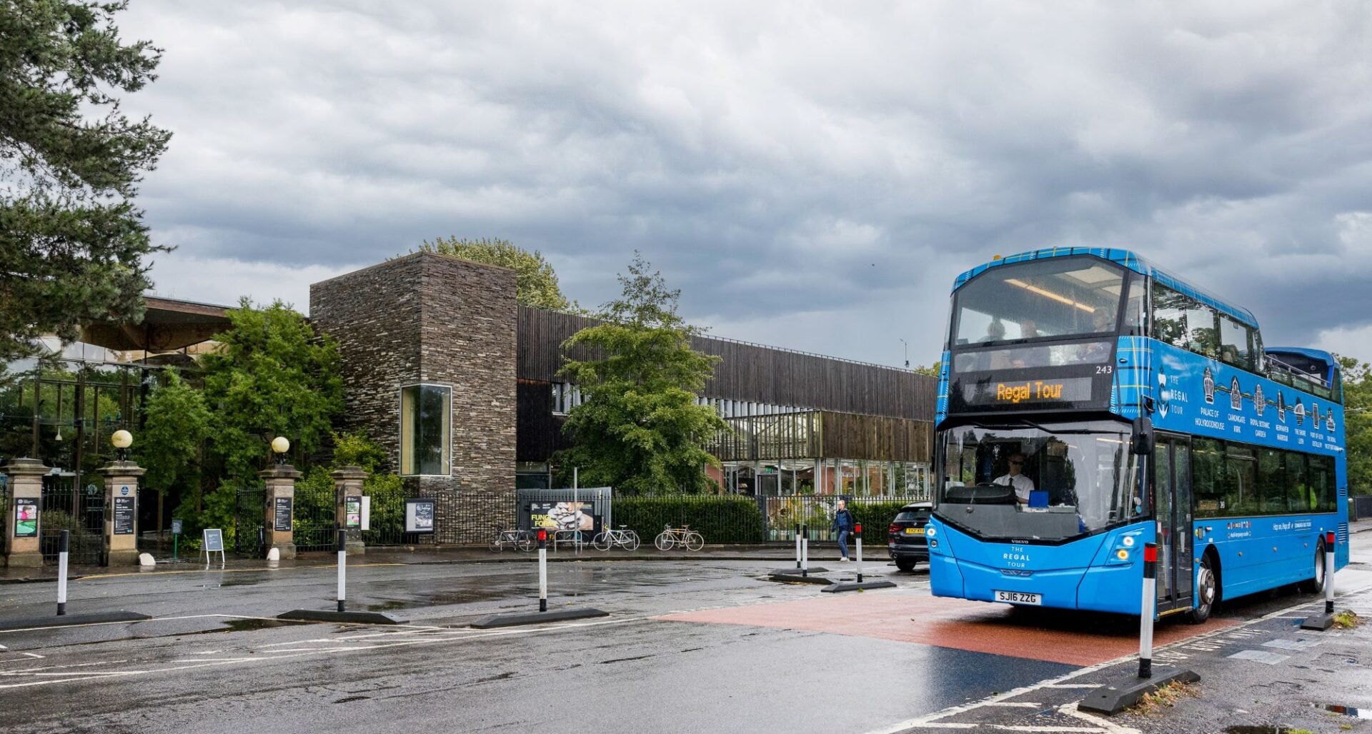 A blue open-top bus tour travelling along a wet street.