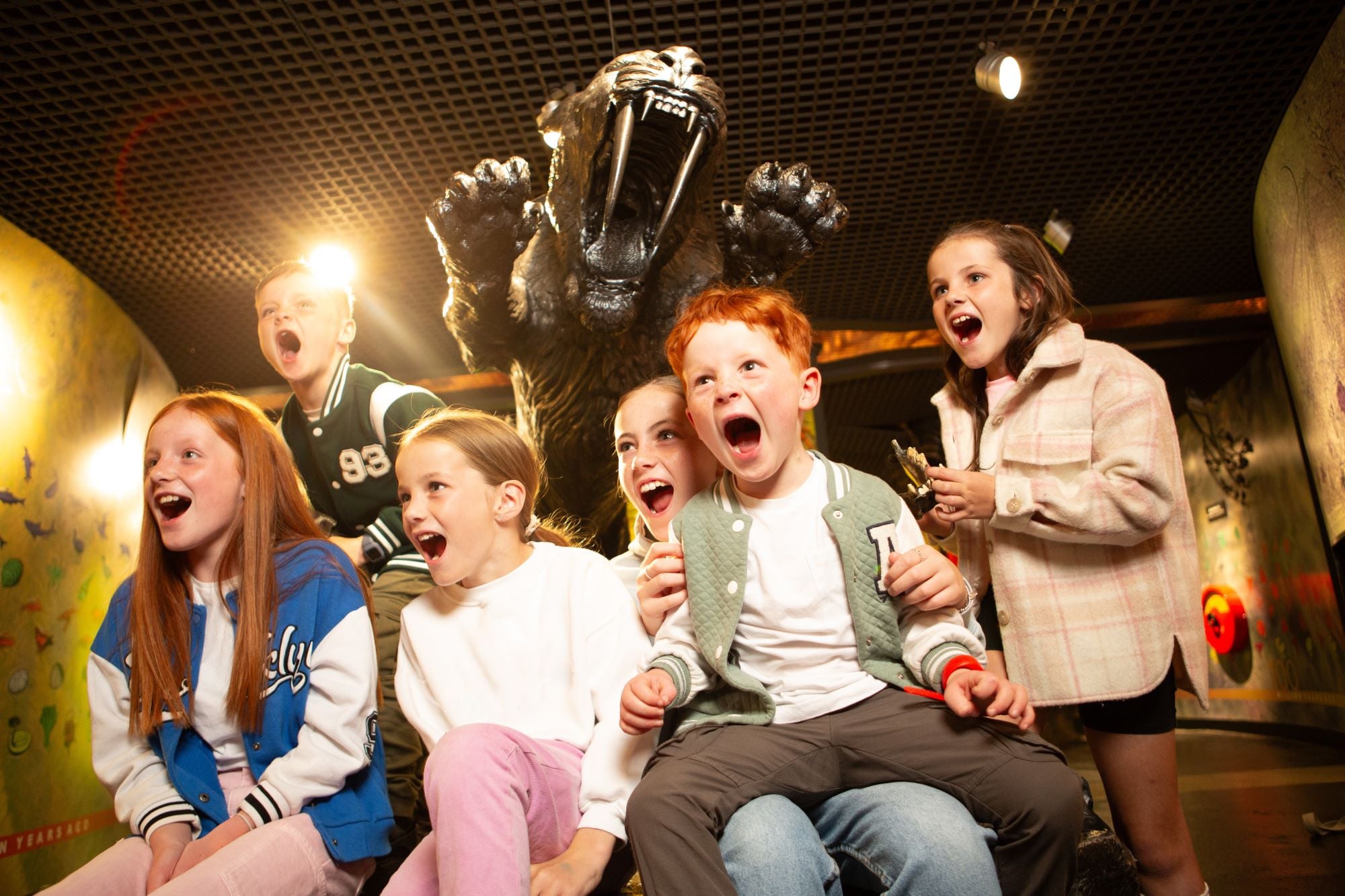 A group of young children, with a model of a sabre-toothed tiger in the background.