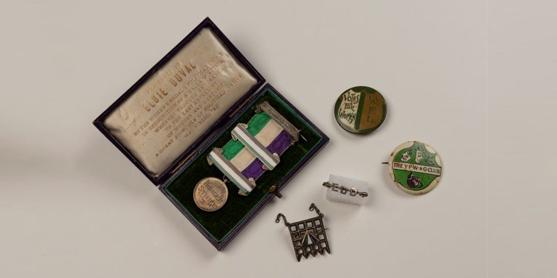 An open leather box, showing a medal, with a green, cream and purple ribbon.