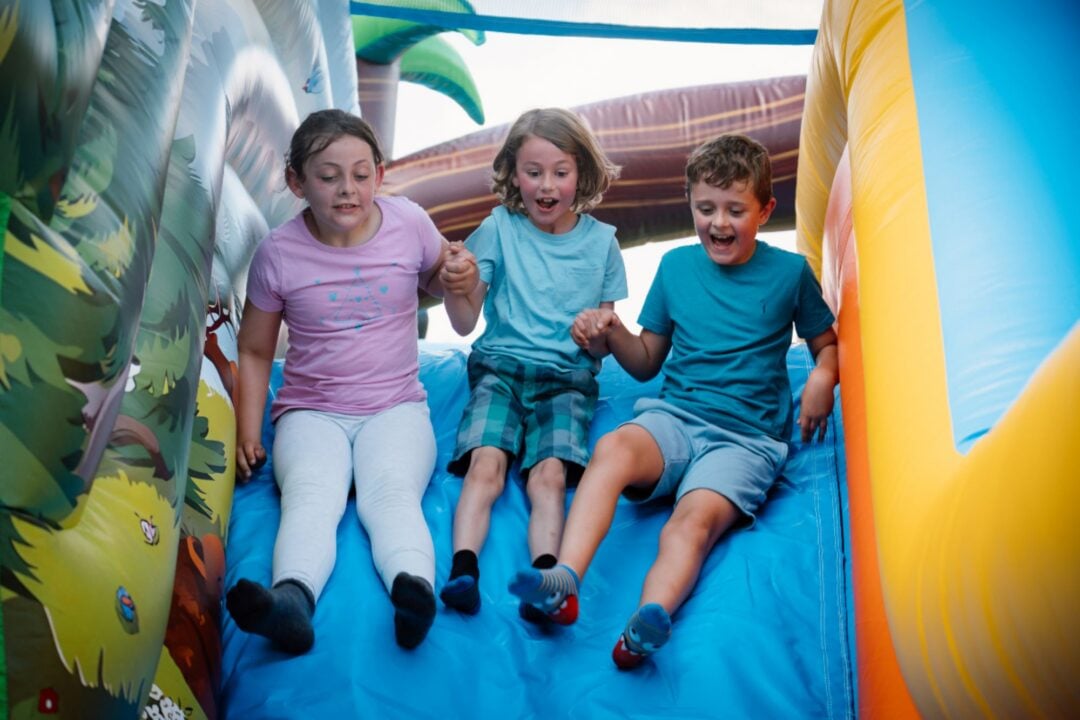 3 young children sliding down an inflatable.